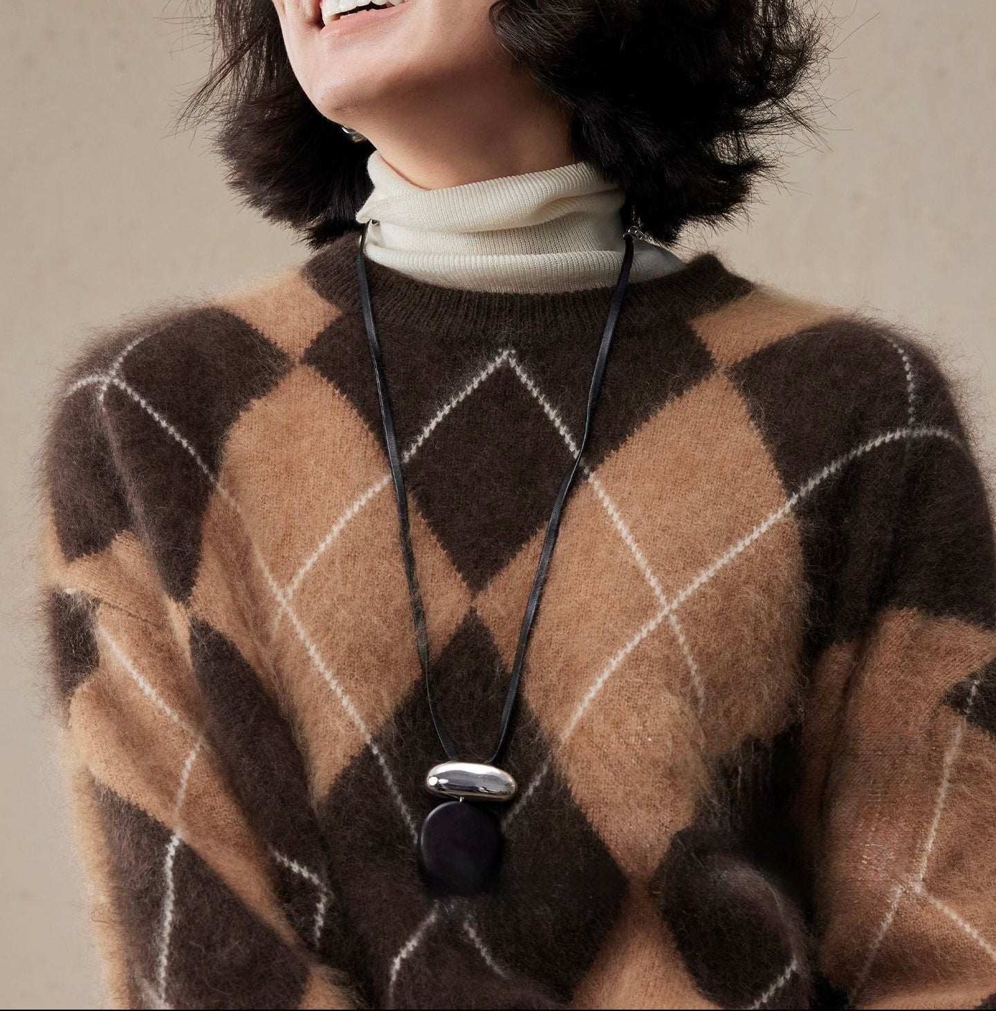 Person wearing a brown and caramel wool sweater with a necklace against a neutral background
