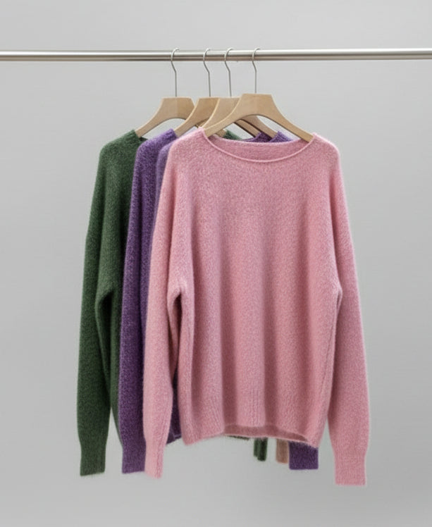 Row of colorful sweaters on hangers against a neutral background